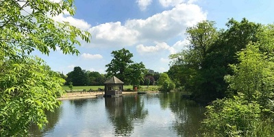 Lake in Dulwich Park surrounded by trees with a hut in the middle