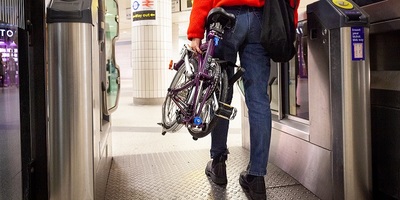 Person walking through ticket gate holding a folded bike