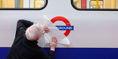 worker revealing underground sign on side of tube train