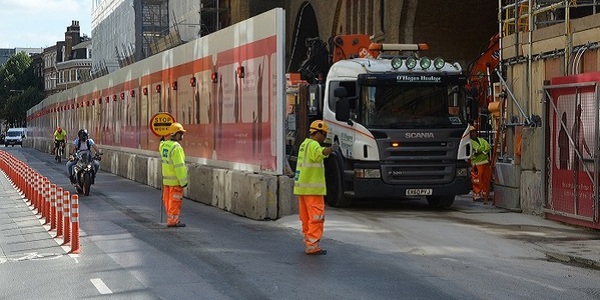 Construction workers directing a lorry out of a construction site whilst traffic is stopped