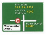 green rectangular road sign with white text and arrows. The top section shows 'City' and 'Peckham' with a straight arrow, the bottom section shows 'Hammersmith' with a right arrow and 'Westminister' with a left arrow and a red and white congestion charge 