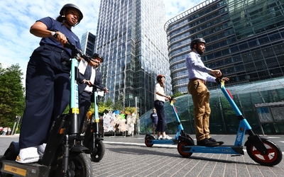 Four people wearing helmets riding on e-scooters